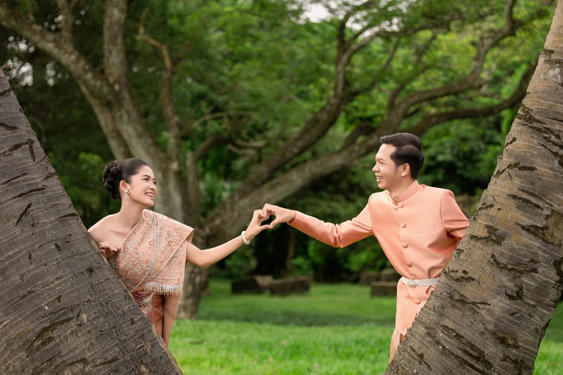 The couple making a heart with their hands between two palm trees
