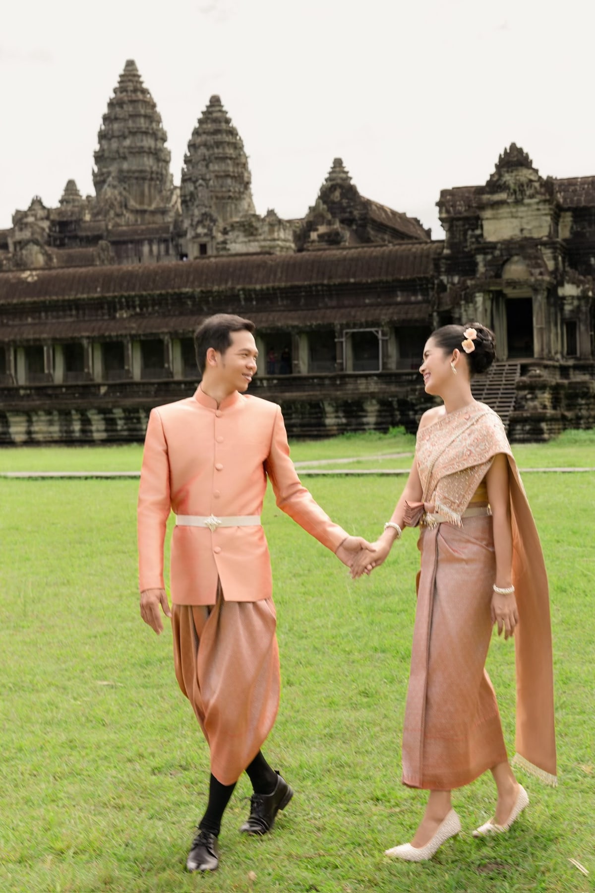 The couple in peach wedding attire holding hands on a temple lawn