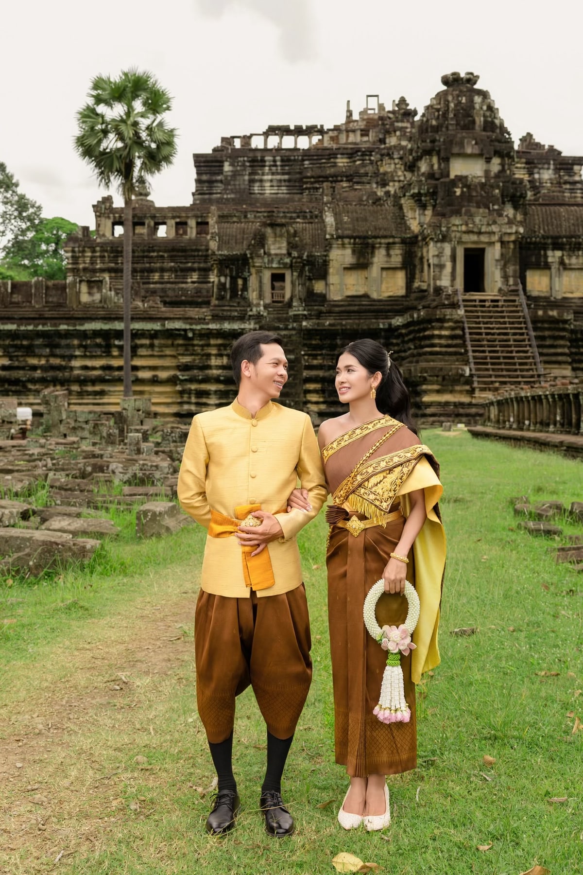 The couple in gold wedding attire in front of a stone temple