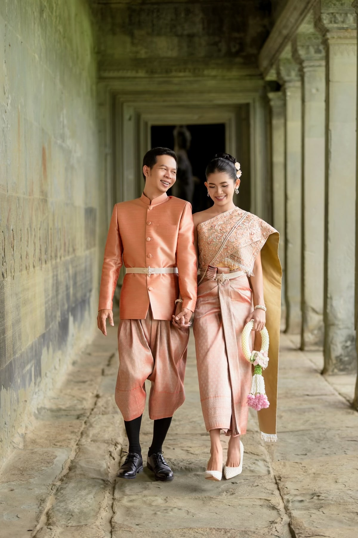 The couple walking hand in hand through a stone corridor